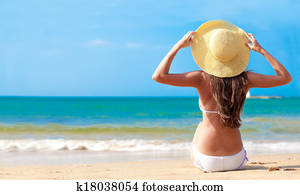 closeup back view young woman in bikini and hat with flower sitting on beach closeup back view young woman in bikini and hat with flower sitting on beach