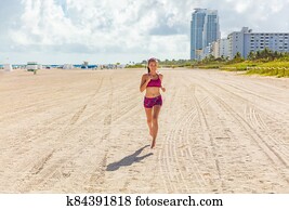 Fit woman training outdoors running barefoot on Miami south beach run jogging workout female Asian athlete. Happy healthy fitness person cardio jog in sun summer lifestyle Fit woman training outdoors running barefoot on Miami south beach run jogging workout female Asian athlete. Happy healthy fitness person cardio jog in sun summer lifestyle