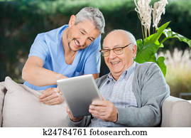 Happy Caretaker And Senior Man Using Tablet PC