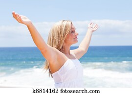 carefree young woman with arms open on beach