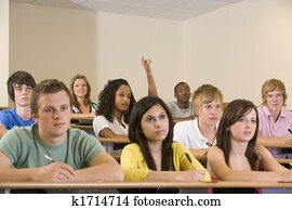Students in class paying attention and taking notes with one volunteering (selective focus)