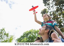 Boy with toy aeroplane sitting on father's shoulders