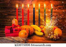 Kwanzaa holiday concept with traditional lit candles, gift box, pumpkins, ears of wheat and miracle magic light on wood background Kwanzaa holiday concept with traditional lit candles, gift box, pumpkins, ears of wheat and miracle magic light on wood background