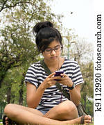 Woman sit on grass sending / receiving a text message / email on her mobile / cellular phone. 