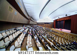 many people are sitting in easy chairs in big conference hall
