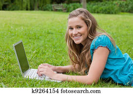 Smiling teenager using her laptop while lying down in a park