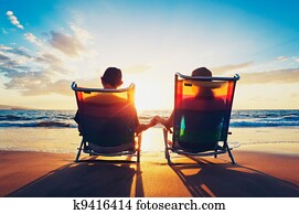 senior couple of old man and woman sitting on the beach watching sunset