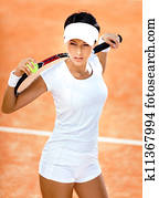 Athletic woman keeps tennis racket and ball on her shoulders