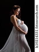 Beautiful brunette model in last trimester posing in studio in sheer white wrap on black background