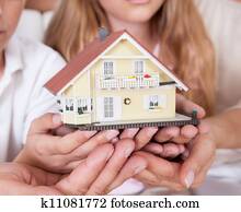Family Sitting Holding Miniature Model Of House