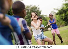 Happy school children playing tug of war with rope in park Happy school children playing tug of war with rope in park