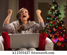Happy woman with laptop rejoicing success in front of Christmas tree
