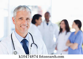 Mature doctor standing upright while waiting for his team