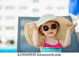 Portrait of baby in hat and glasses sitting on sun bed
