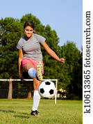 Teen girl kicking soccer ball on field