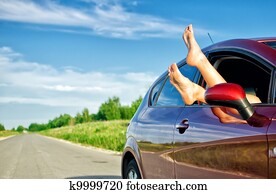 Woman's legs out of the car window. Concept of carefree funny trip.