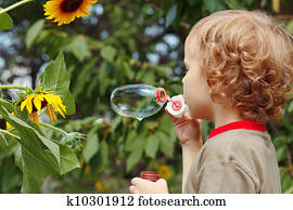 Young blond boy blowing a bubbles outdoors on a sunny day