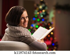 Happy young woman reading book in front of Christmas tree