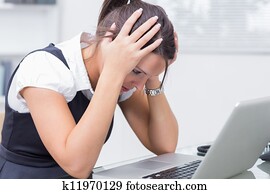 Side view of frustrated young business woman with head in hands in front of laptop at office desk