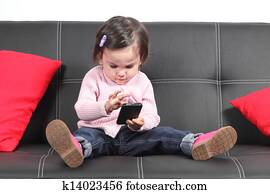 Casual baby sitting on a couch touching a mobile phone
