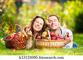 Couple Relaxing on the Grass and Eating Apples in Autumn Garden Couple Relaxing on the Grass and Eating Apples in Autumn Garden