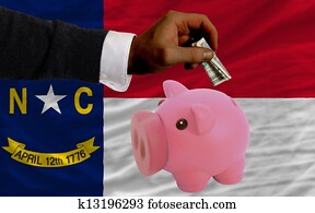 Man putting dollar into piggy rich bank flag of us state of north carolina in foreign currency because of inflation