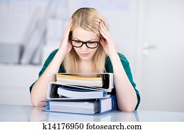 Overworked Businesswoman Looking At Stack Of Binders At Desk