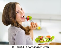 Smiling young woman eating fresh salad in modern kitchen