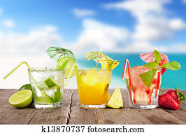 Summer cocktails with pieces of fruit on wooden table. Blur beach on background Summer cocktails with pieces of fruit on wooden table. Blur beach on background