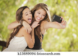 Two Attractive Mixed Race Girlfriends Taking Self Portrait with Their Phone Camera Outdoors.