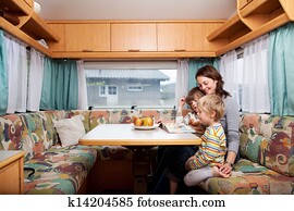 Woman With Sons Reading Story Book At Table In Caravan