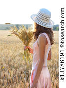 Young girl in the hat and pink dress holding wheat ears in her hand against a background of wheat field. Concept of abundance