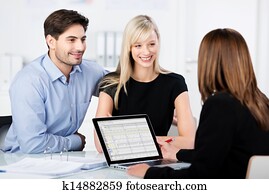 Couple Smiling While Looking At Financial Advisor At Desk Couple Smiling While Looking At Financial Advisor At Desk