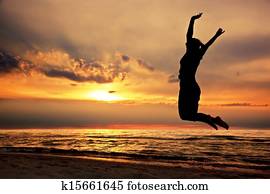 Happy woman jumping on the beach at sunset