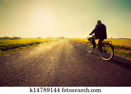 Old man riding a bike to sunny sunset sky