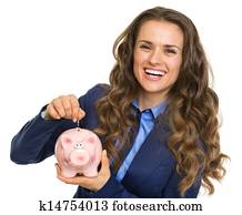 Smiling business woman putting coin into piggy bank