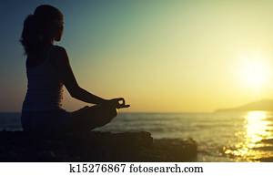 yoga outdoors. silhouette of a woman sitting in a lotus position on the beach at sunset