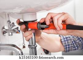 Young plumber fixing a sink in bathroom Young plumber fixing a sink in bathroom