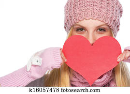 Happy girl in winter clothes hiding behind heart shaped valentines postcard