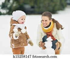 Happy mother and baby making snowman in winter park