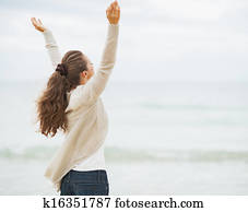 Happy young woman in sweater rejoicing on beach . rear view