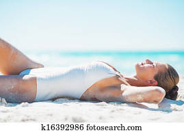 Happy young woman in swimsuit tanning on beach