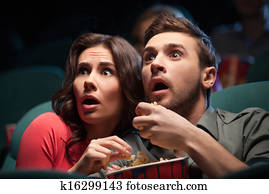 Horror movie. Terrified young couple eating popcorn while watching movie at the cinema Horror movie. Terrified young couple eating popcorn while watching movie at the cinema
