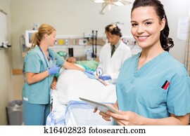 Portrait of nurse with digital tablet while doctor and colleague operating male patient in hospital