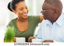smiling elderly african american man enjoying coffee with his granddaughteer at home