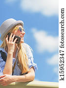 Smiling hipster girl talking mobile phone and looking on copy space against sky