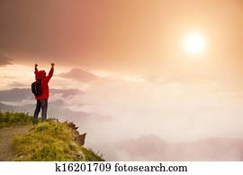 Young man with backpack standing  on top of  mountain watching the sunrise