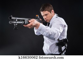 Bodyguard. Serious young man in shirt and tie holding gun and aiming somewhere while standing against black background