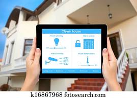 Female hands hold a tablet computer with system clever house on a screen on the background of the house