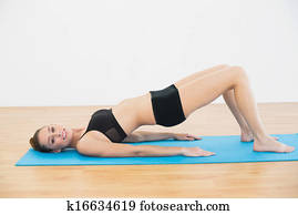Gleeful young woman in sportswear lying on exercise mat doing exercises smiling at camera